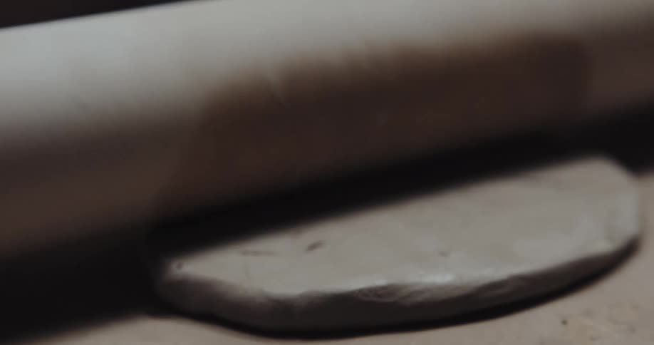 A rolling pin is moving over a circle of dough on a board