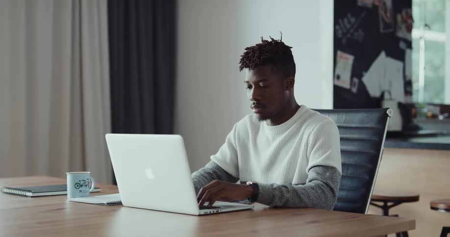 A man is sitting indoors and browsing on his laptop