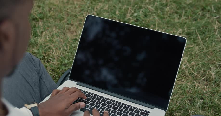A person is typing on their laptop and sitting outdoors