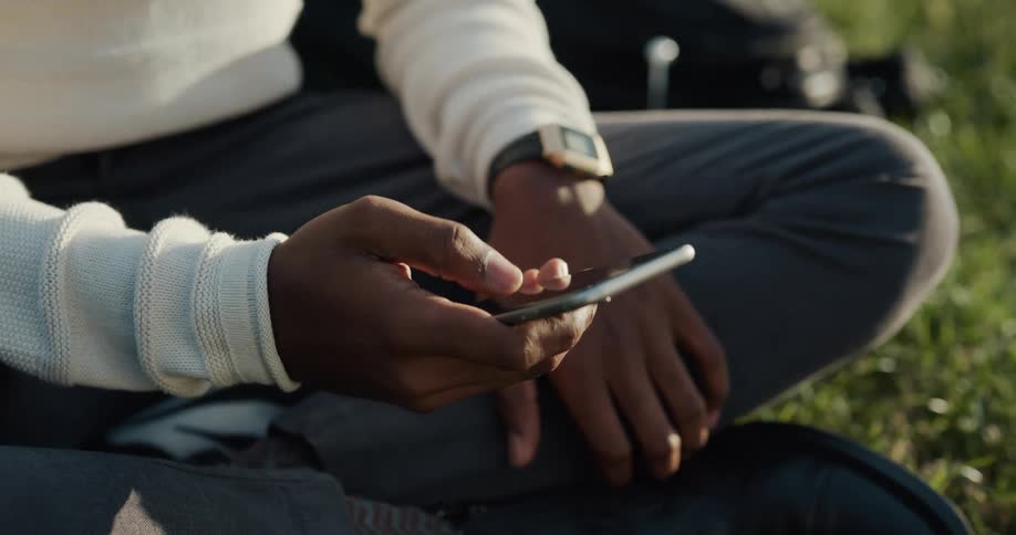A man is sitting outside on the grass using his cell phone