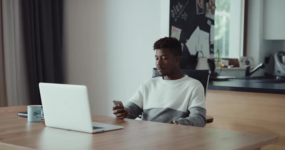 A man is sitting at a table with his phone and laptop