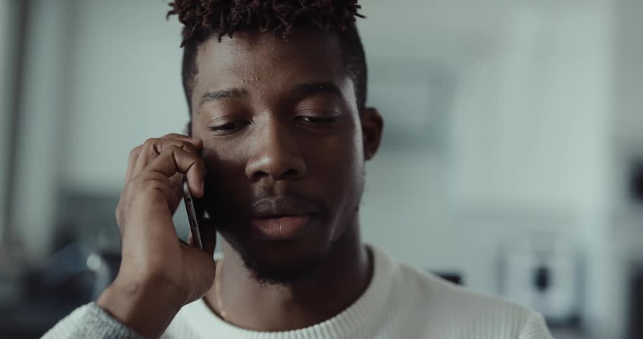 Black man sitting indoors picking up a phone call