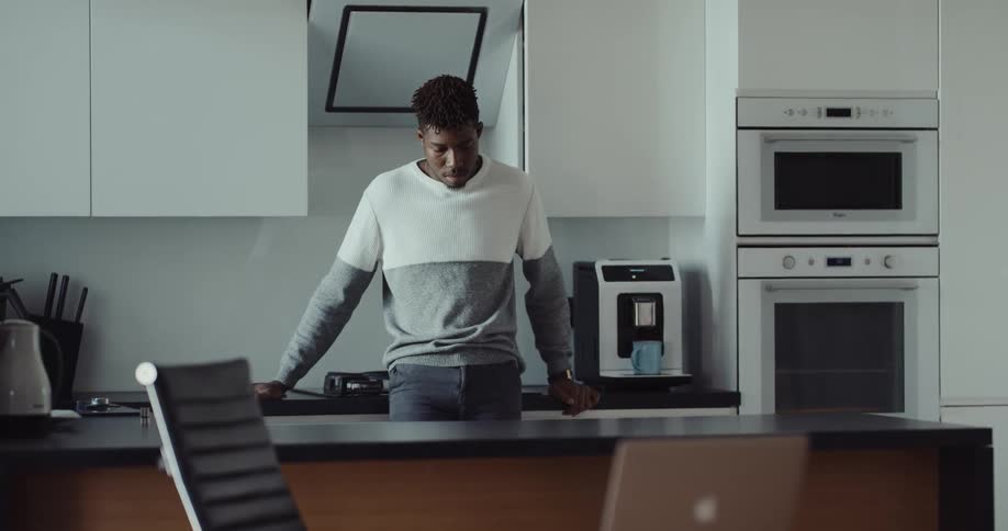Man with beard and gray and white sweater holds cup in the kitchen