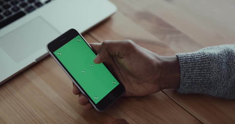 A person uses their thumb to swipe and tap the screen of a smartphone while sitting at a table indoors