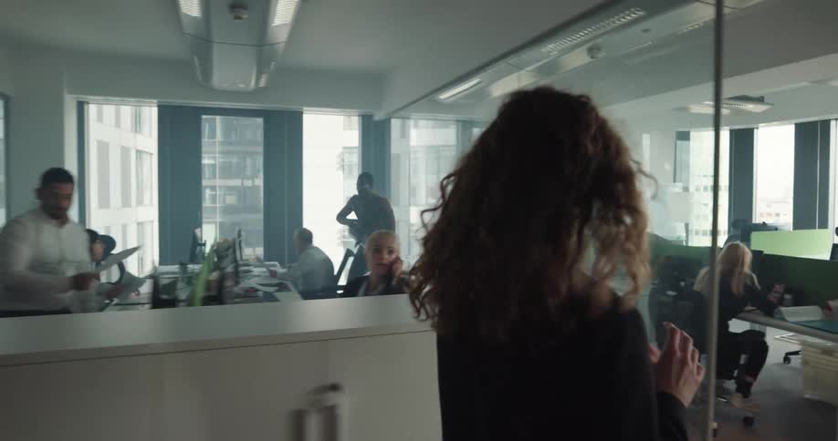 Woman walks into office with floor to ceiling windows that show other buildings