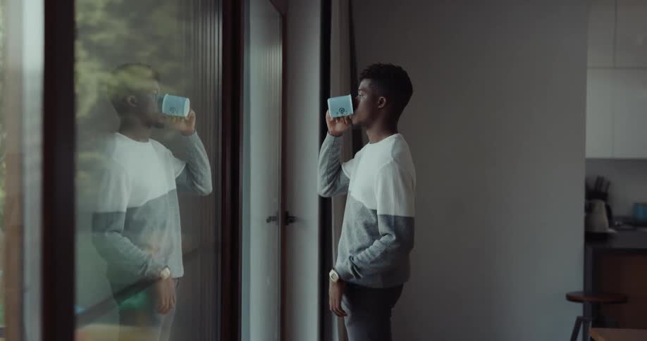 A man is drinking coffee and looking out a window