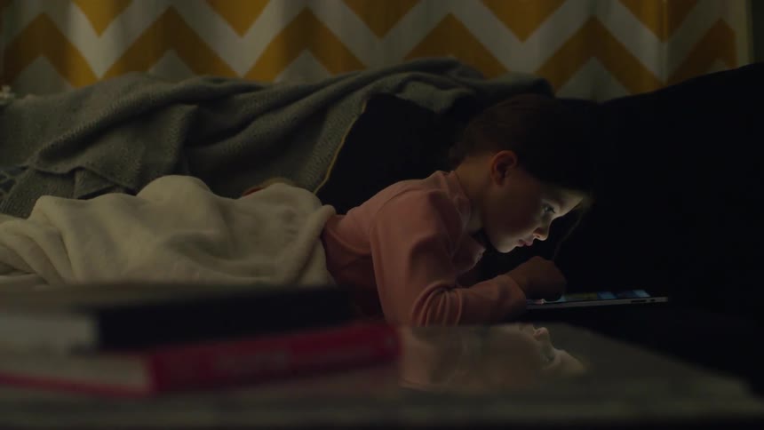 A child looks at a tablet while laying down