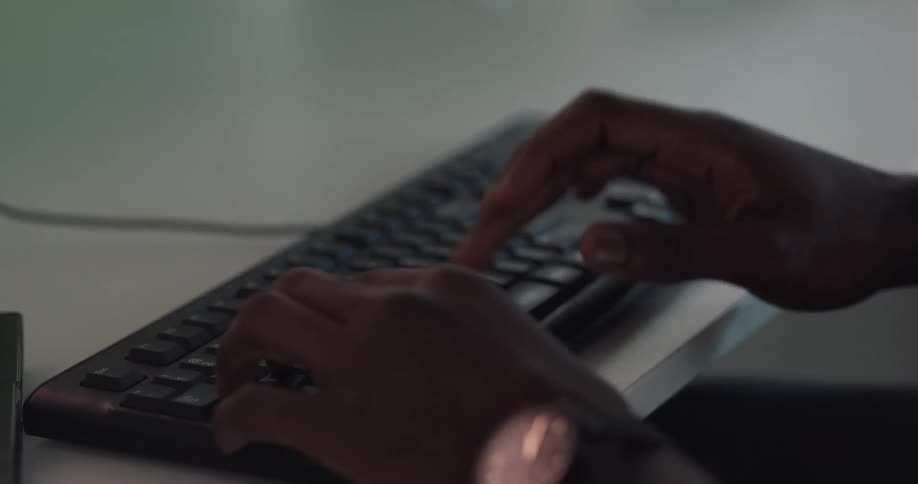 Concentrated black man sitting at the desk in an office typing on a computers keyboard