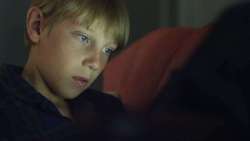 A young boy plays on a tablet in his pajamas