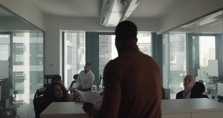 An office supervisor hands out paper work to the employees hes speaking to in a conference room