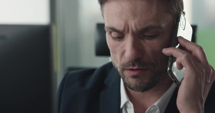A man is sitting in an office and talking on a cellphone