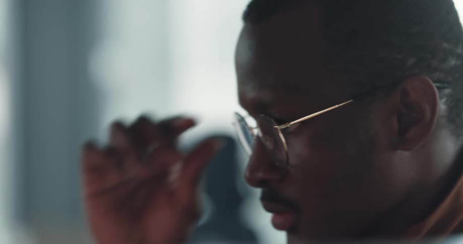 A man is standing indoors and wearing glasses