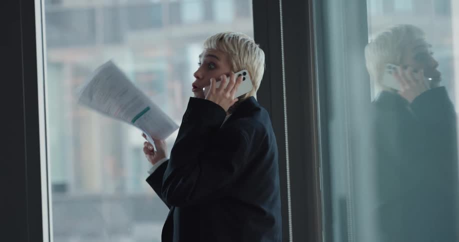 Woman with blonde short hair and blazer jacket talks on smartphone in the office