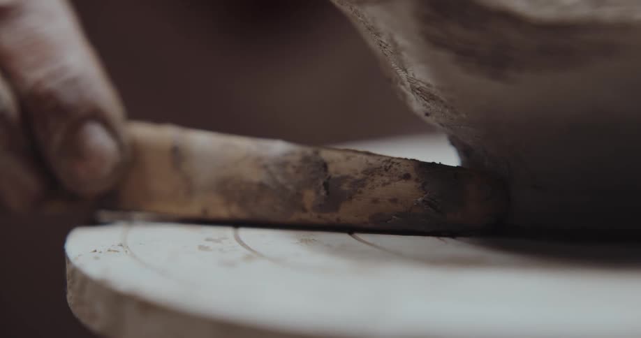 A person uses a tool to shape clay on a pottery wheel