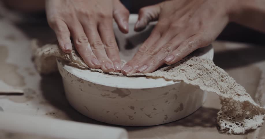 Person presses lace onto clay plate sitting in form to create pattern