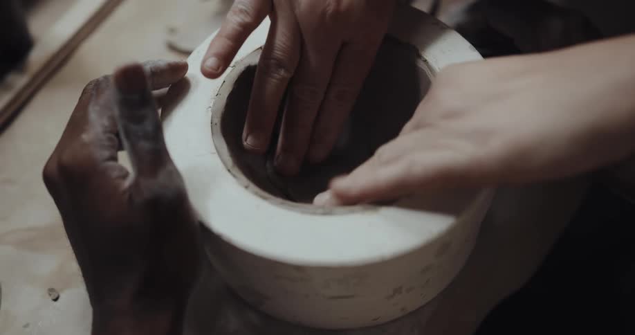 Woman scores bottom of clay in form and adds piece that second potter smooths in