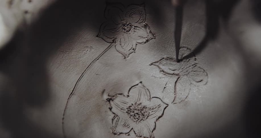A person is carving flowers into the clay