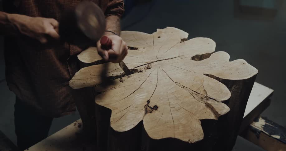 A man uses a mallet and chisel to carve a tree stump
