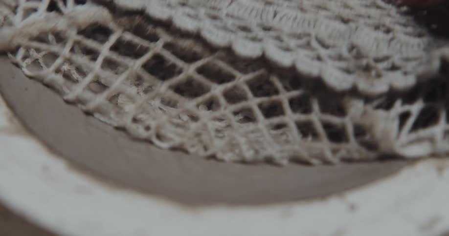 Person presses lacy fabric into clay bowl to create a pattern
