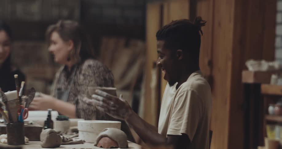 People laugh and talk while sitting in pottery studio working on different projects