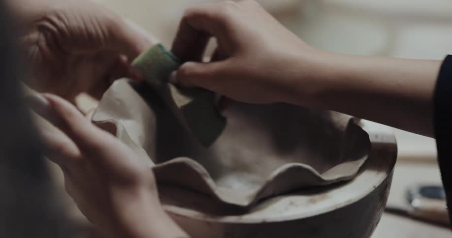 Two people are working to shape a pottery bowl