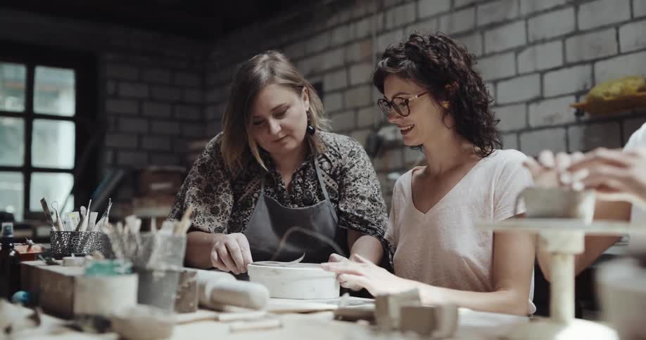 Pottery class instructor helps student work in clay