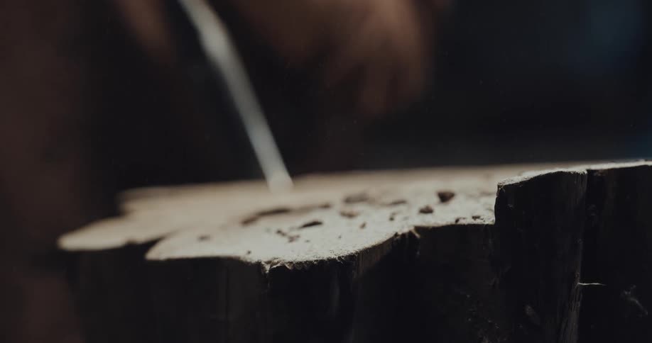 Person carves wood with a metal tool and blows off the dust