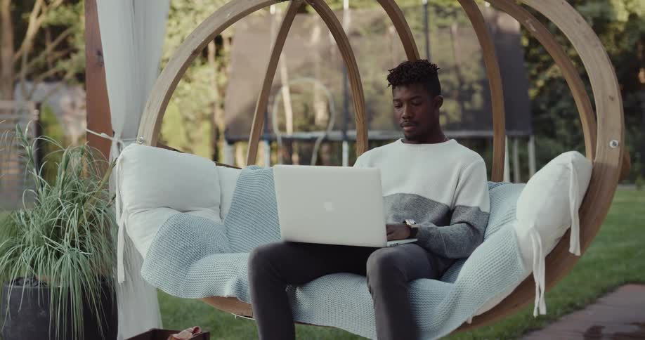 A man is sitting on outdoor furniture with his laptop