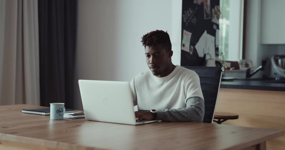A man sits down at a table and types on a laptop computer