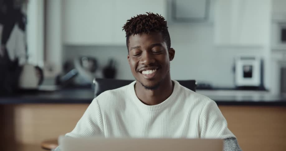 A man is sitting by his laptop and smiling
