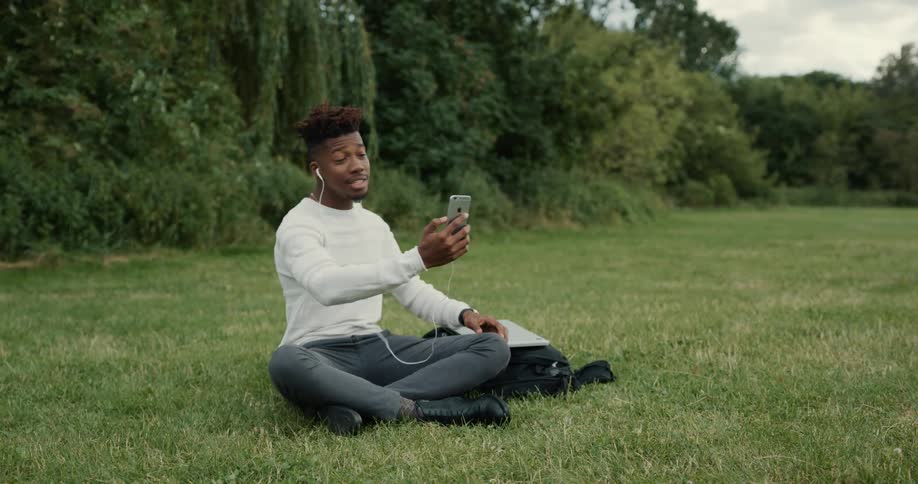 A man sits in a large open lawn area talking on a cell phone