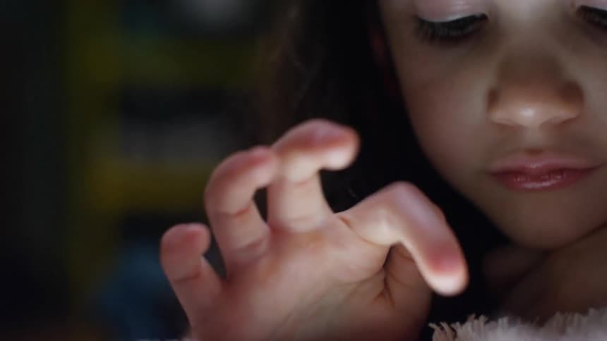 A child plays on a tablet sitting on a bed