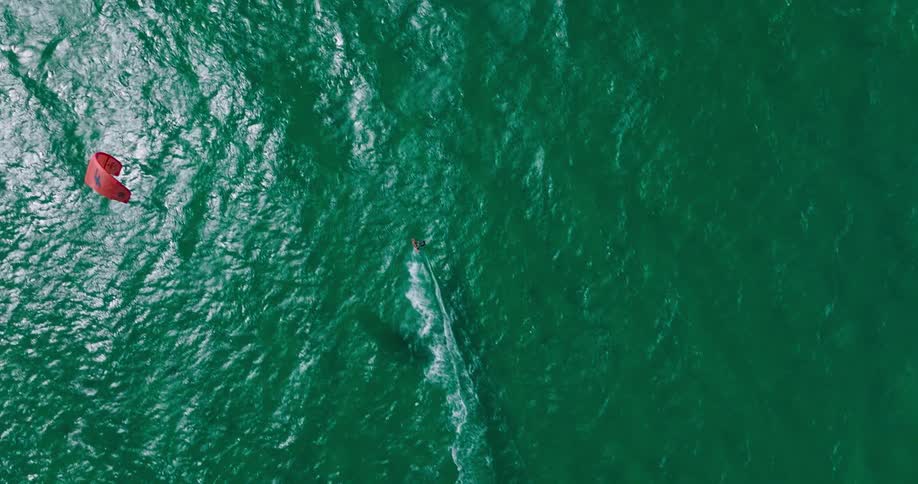 A person is moving through the water on a kite board as a jet ski rides past