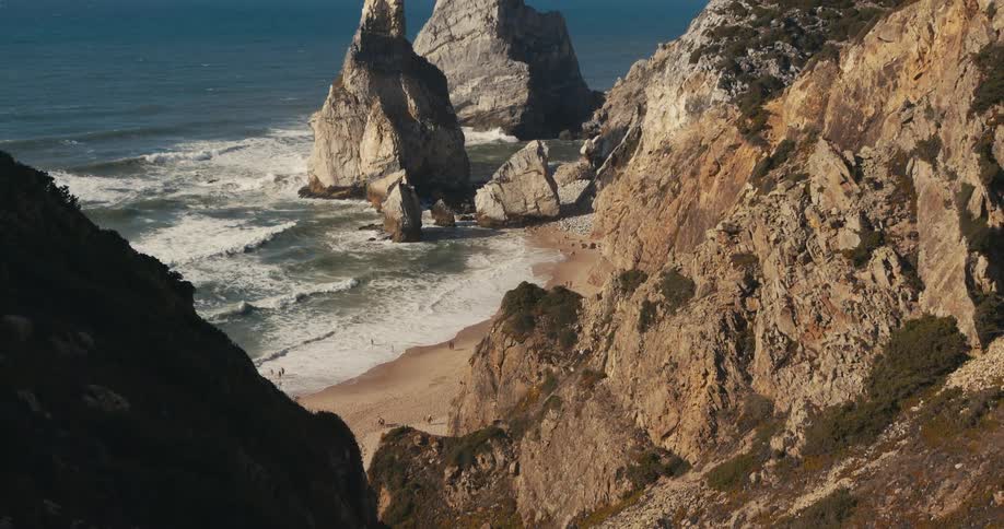 A beach at the bottom of a rocky mountain slope during the day