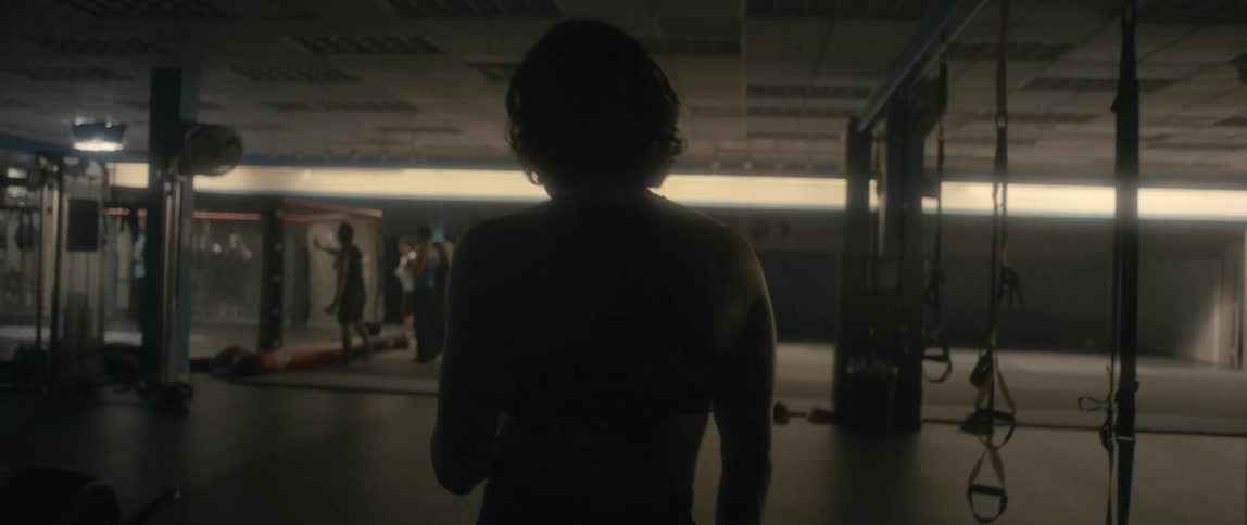 Silhouette of a female boxer putting a mouthguard while walking inside a dimly lit gym