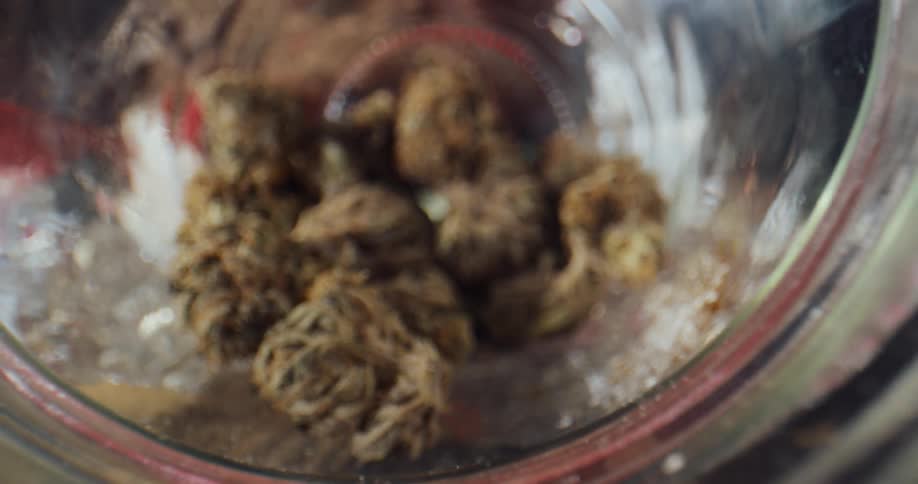 Marijuana buds are inside a jar on a table