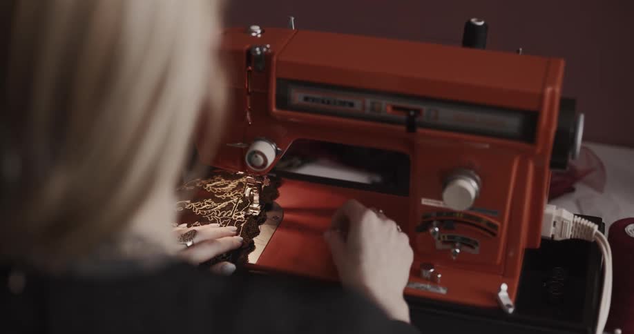 A woman sews fabric using a sewing machine at a table indoors
