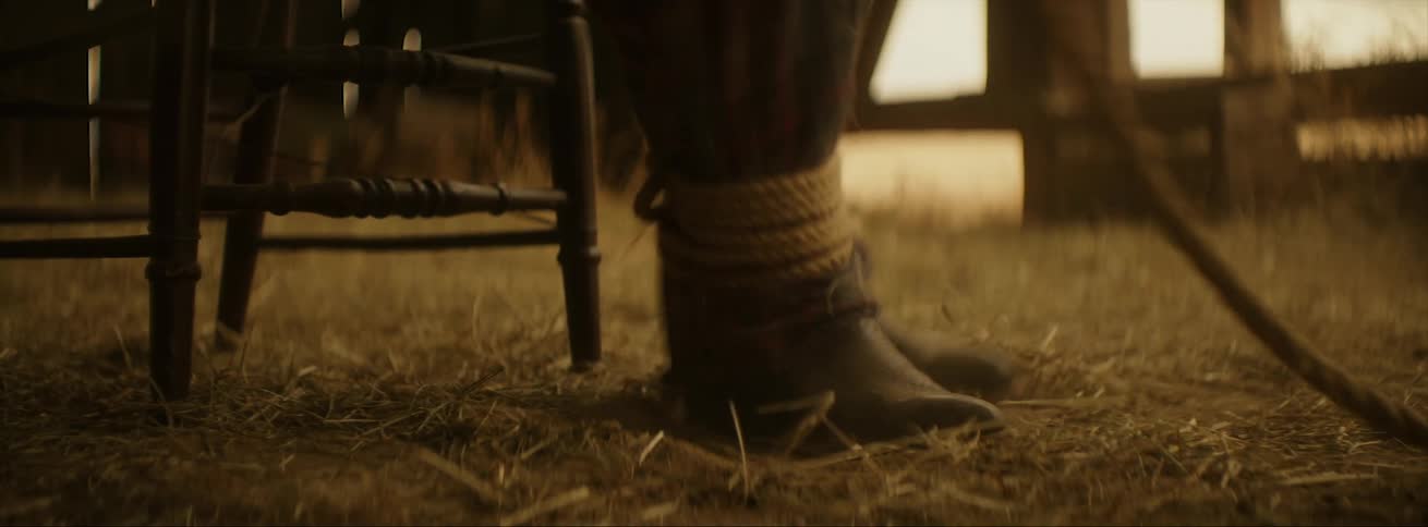 Person tied to a chair with rope inside a barn struggling to get free