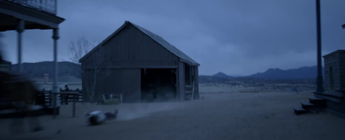 Aerial view of a cowboy on a horse dragging a person through a town at evening