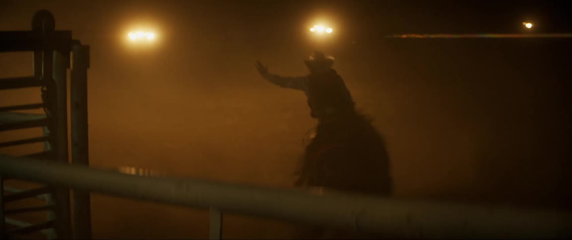 A man is riding a bull in a stadium during the night time