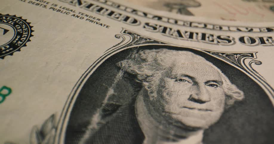A dollar bill sits on a stack of other bills