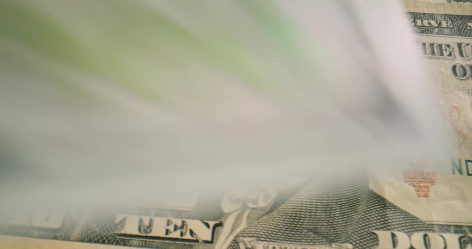 American bank notes fall onto a black surface one by one