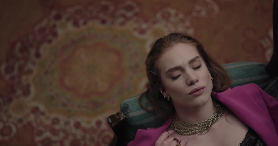 Woman leisurely resting reclined on a couch next to an elaborate rug