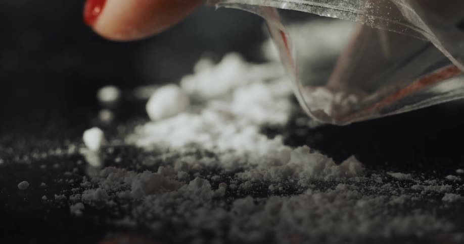 A person sprinkles white cocaine powder over a mirror