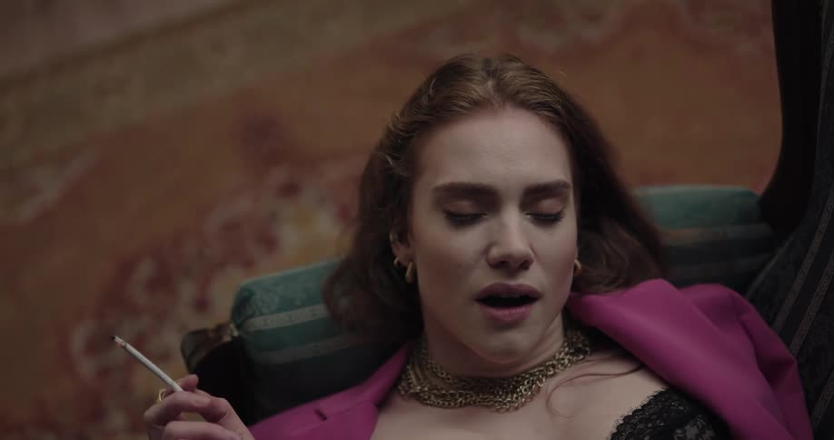 Thoughtful young beautiful woman wearing jewelry lying on the couch smoking a cigarette
