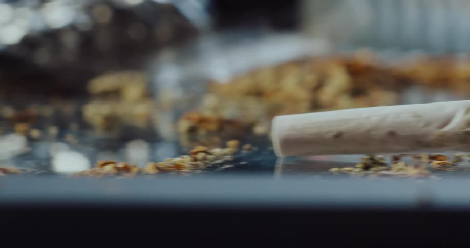 Close up of a marijuana cigarette laying over a table surrounded by drug paraphernalia