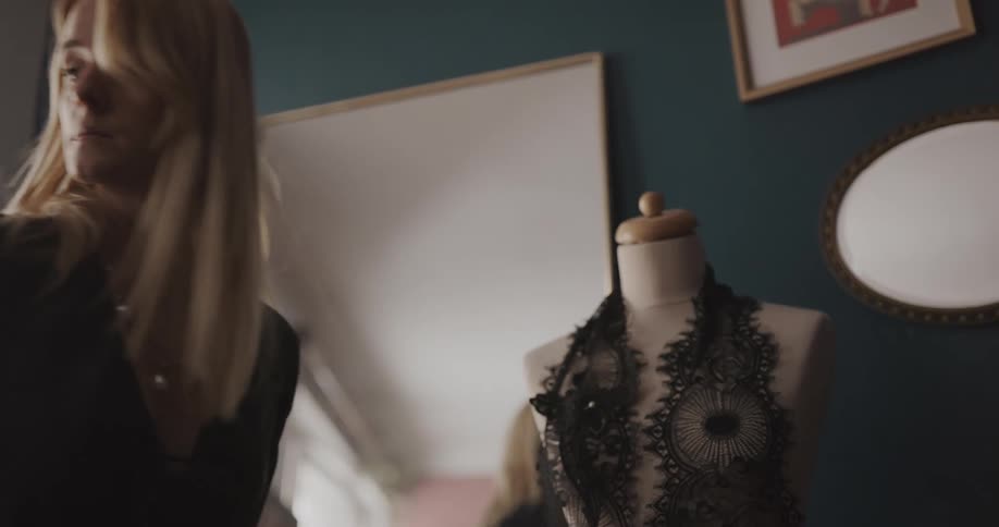 A woman in a dress shop is creating an article of clothing on a mannequin