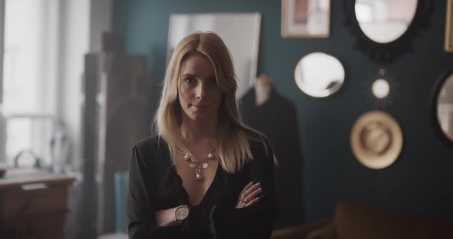 Long haired blonde woman standing on a room turns around to look at the camera