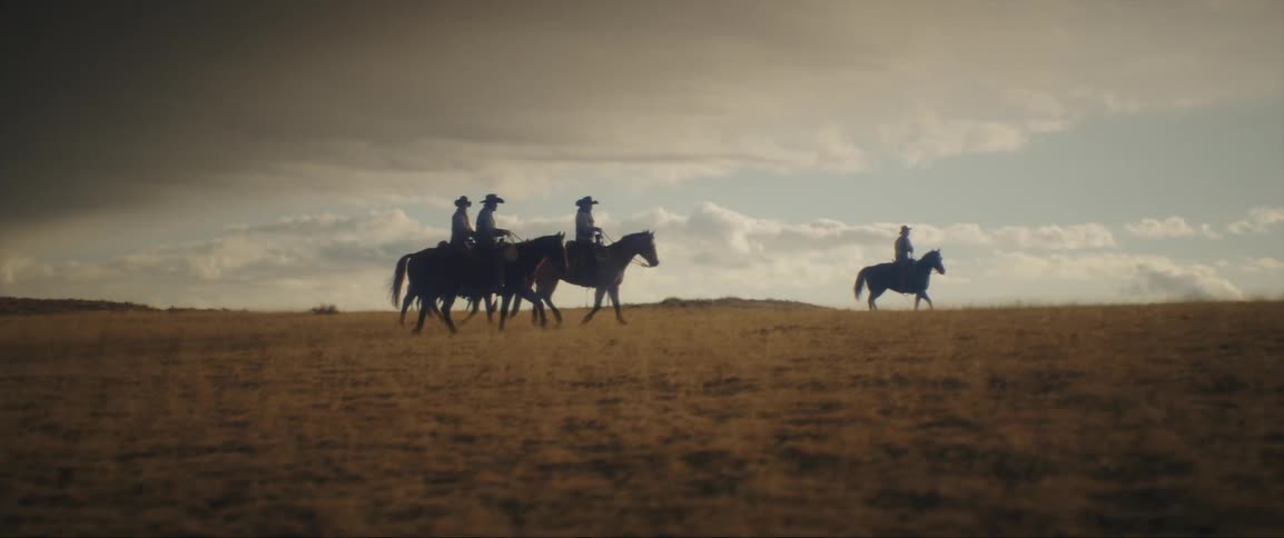 Silhouette of a group of cowboys riding on horses through the plains at evening