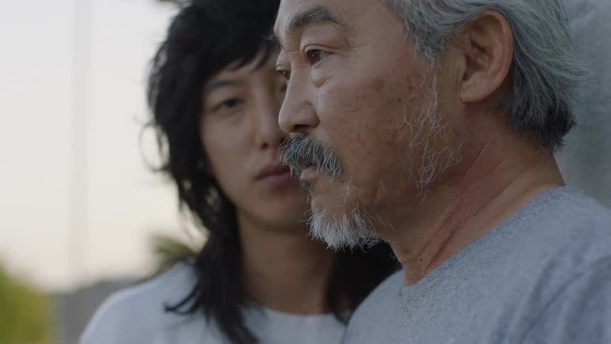 An asian father and son stand together outside